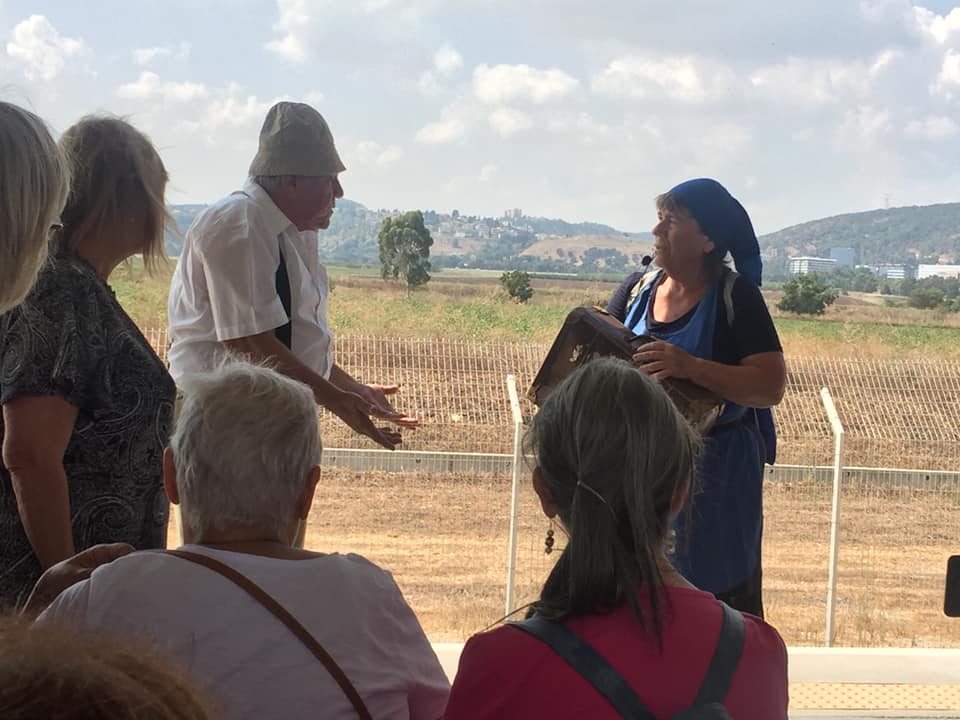 אנשים עומדים בחוץ בשדה, מקשיבים לגבר בכובע מדבר במהלך דיון.