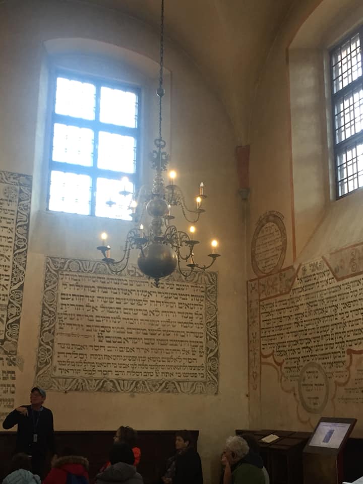 פנים היסטורי עם נברשת, חלונות גבוהים, כתובות על הקיר ואנשים יושבים למטה