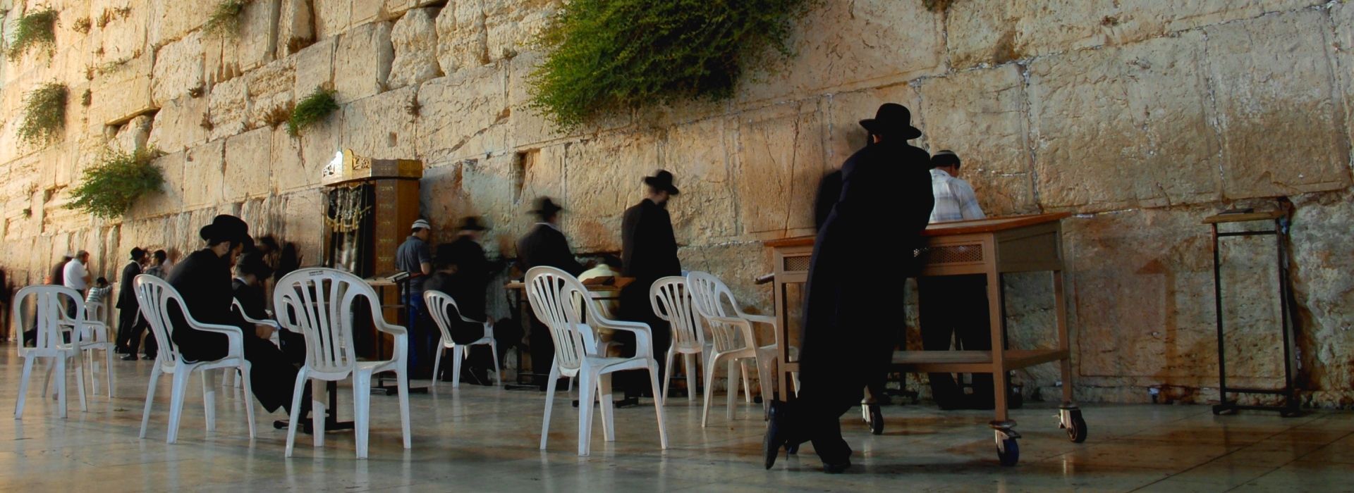 אנשים יושבים בשולחנות חיצוניים ליד קיר אבן גדול, כשמלצר עומד בקרבת מקום.
