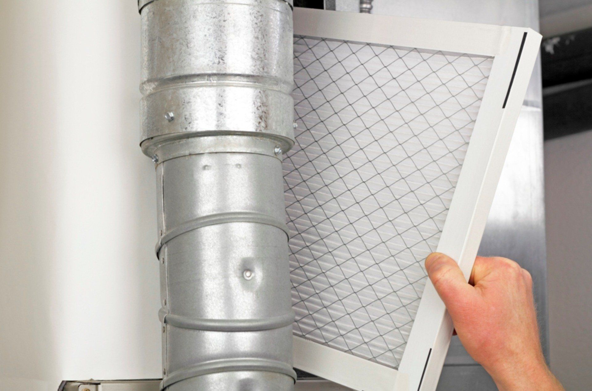 A person is holding a filter next to an HVAC duct