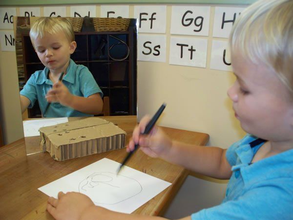 A young boy is drawing on a piece of paper in front of a mirror