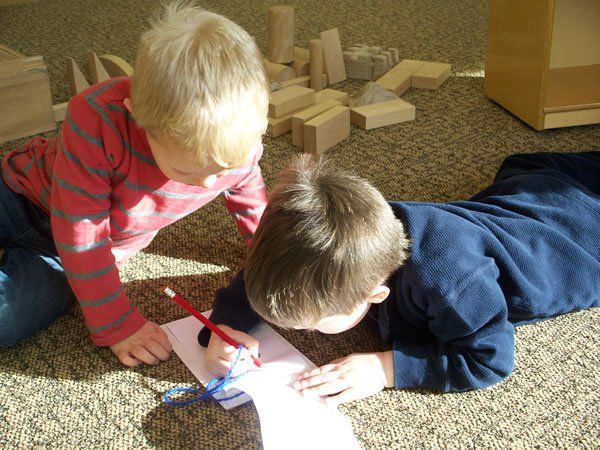 Two young boys are laying on the floor writing on a piece of paper