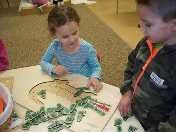 A boy and a girl are playing with a puzzle that looks like a crocodile