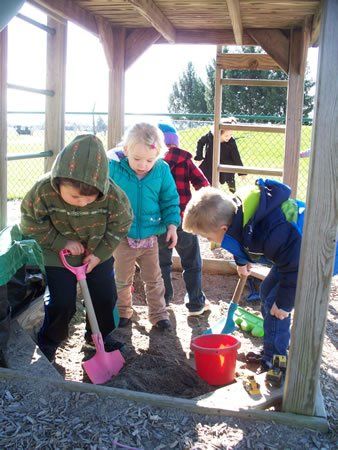 A group of children are playing in a sandbox with shovels and buckets.