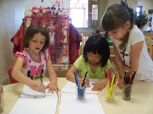 Three little girls are sitting at a table drawing with markers