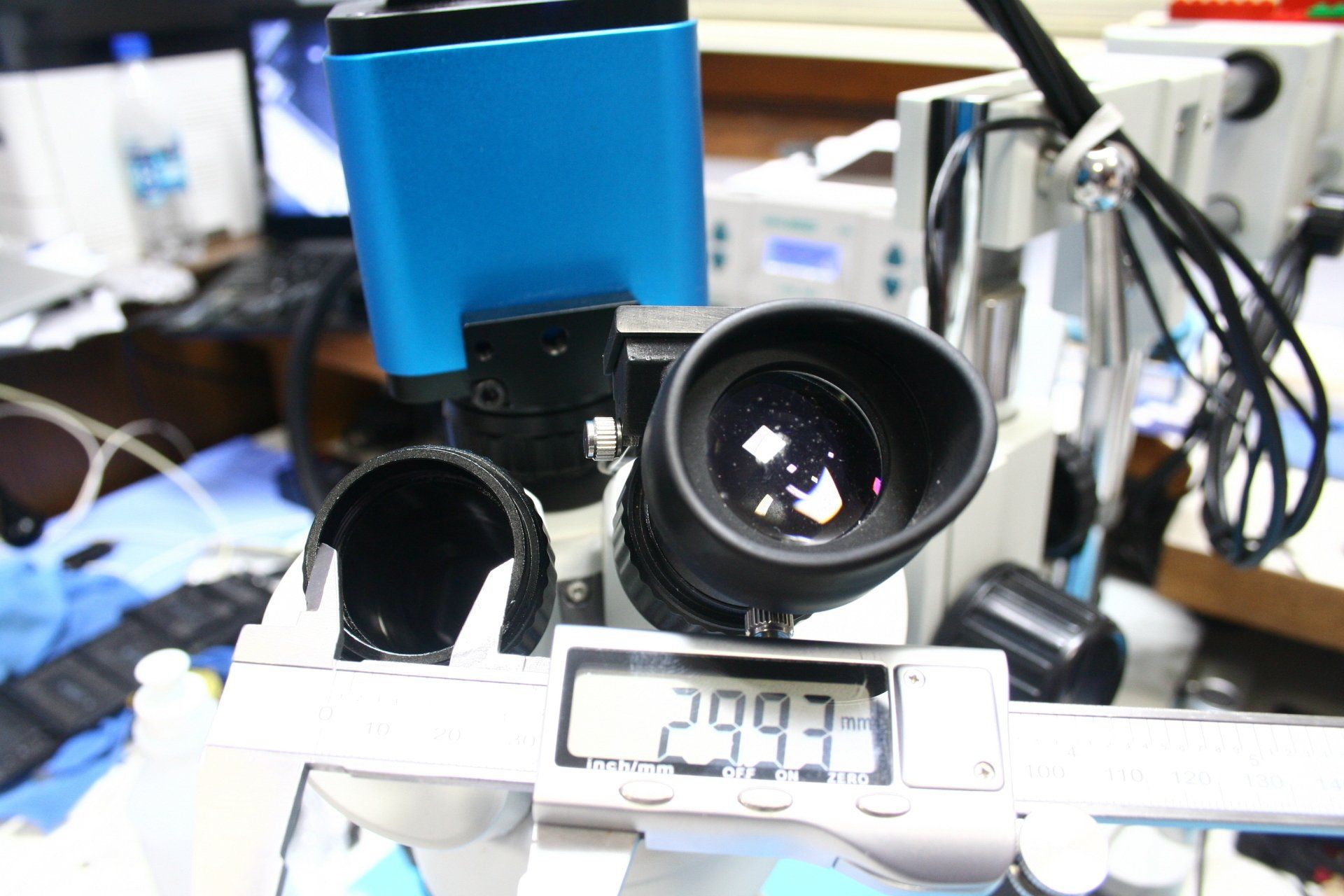 A microscope is being measured by a digital caliper showing 29.93mm