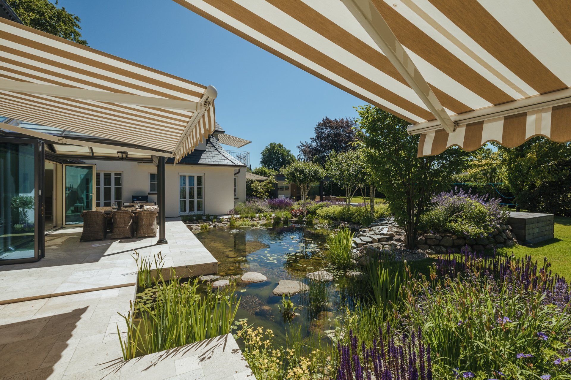 Eine Terrasse mit einer gestreiften Markise darüber und einem Teich im Hintergrund
