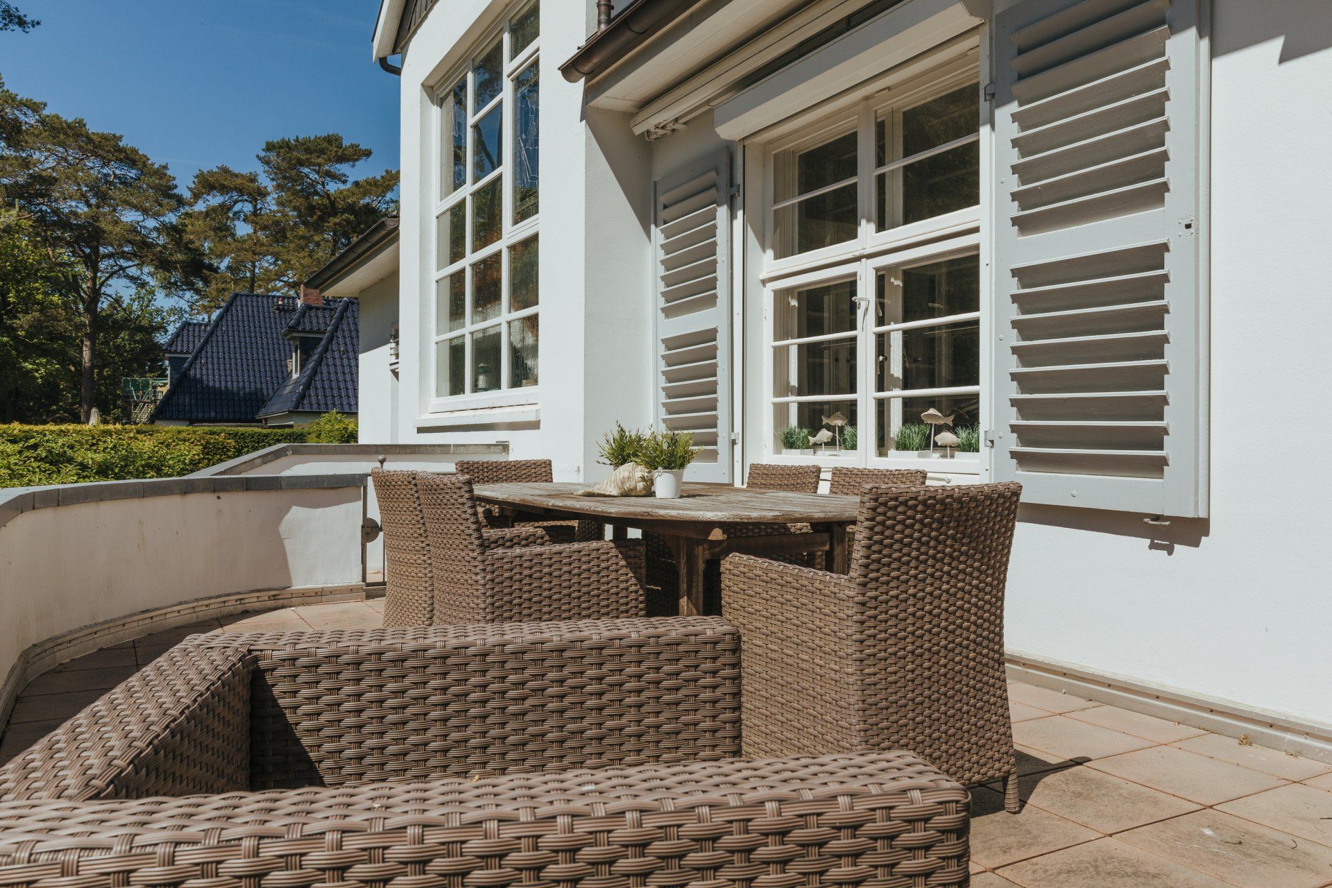 Eine Terrasse mit Korbmöbeln und einem Tisch und Stühlen vor einem weißen Haus.