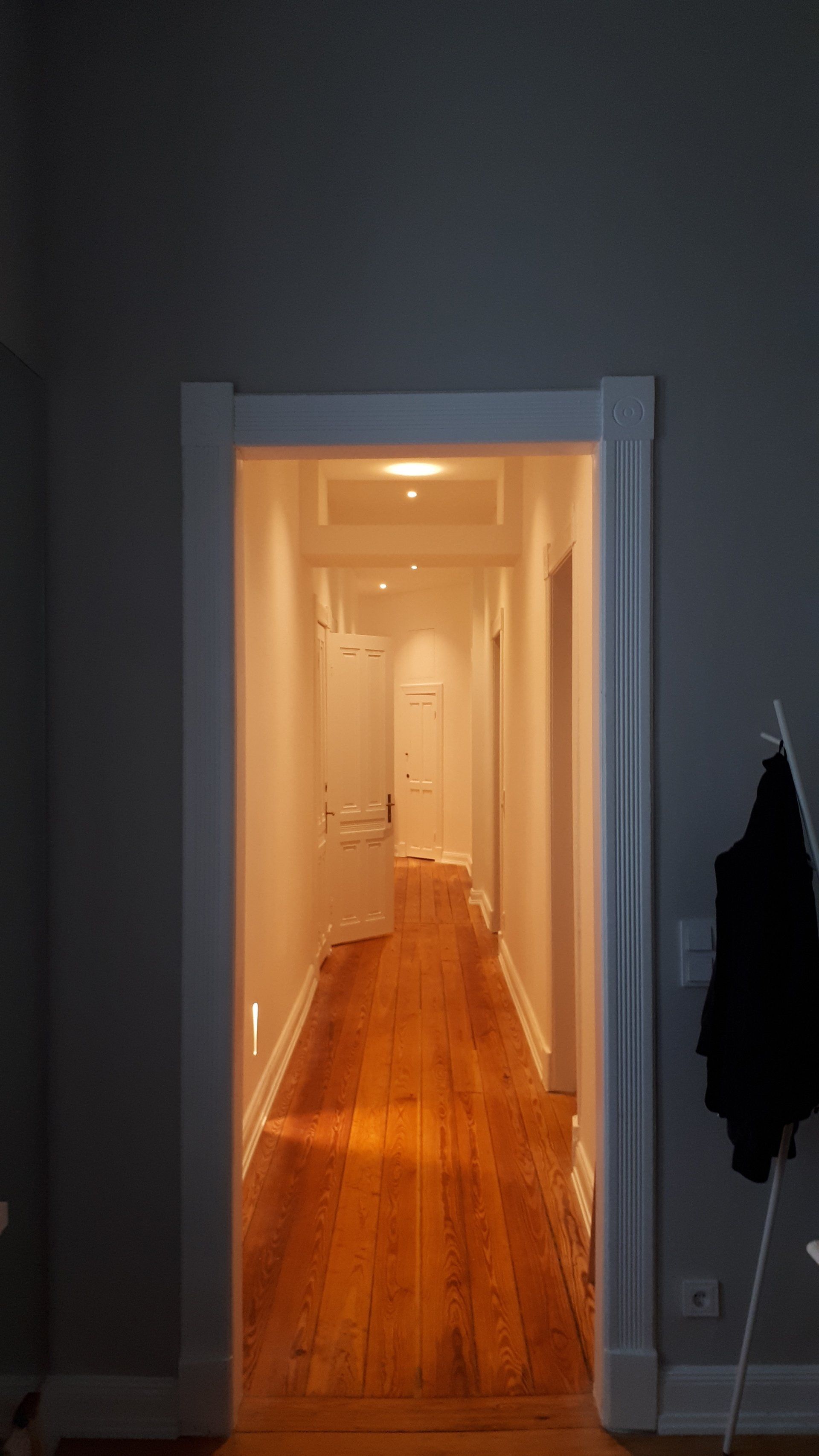 Ein langer Flur mit Holzboden und weißen Wänden in einem Haus.
