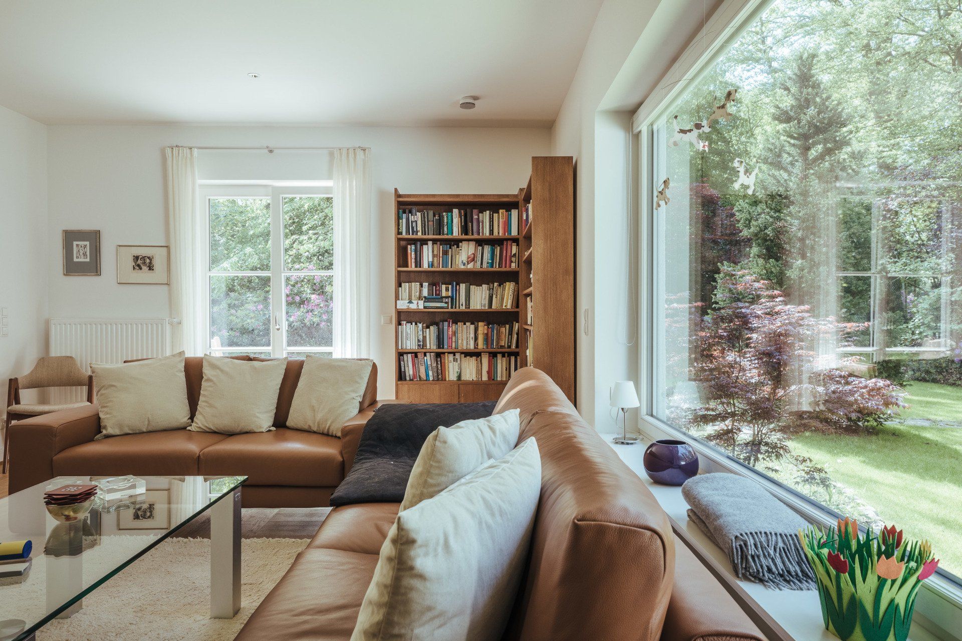 Ein Wohnzimmer mit Couch, Couchtisch, Bücherregal und großem Fenster.