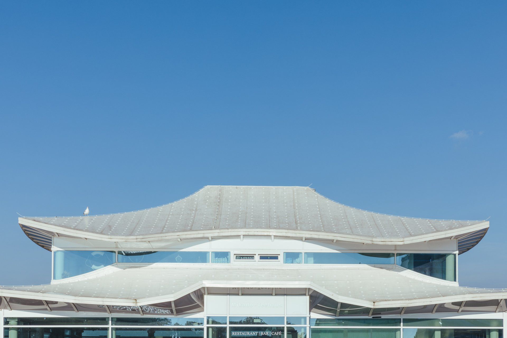 Ein großes Gebäude mit einem geschwungenen Dach und einem blauen Himmel im Hintergrund.