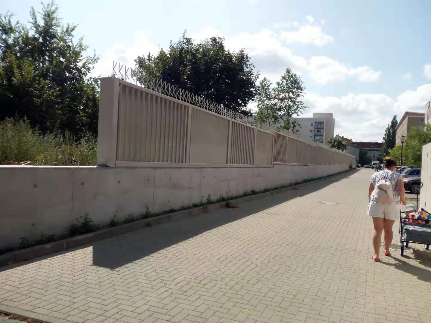 Eine Frau geht auf einem Gehweg neben einem Zaun entlang.