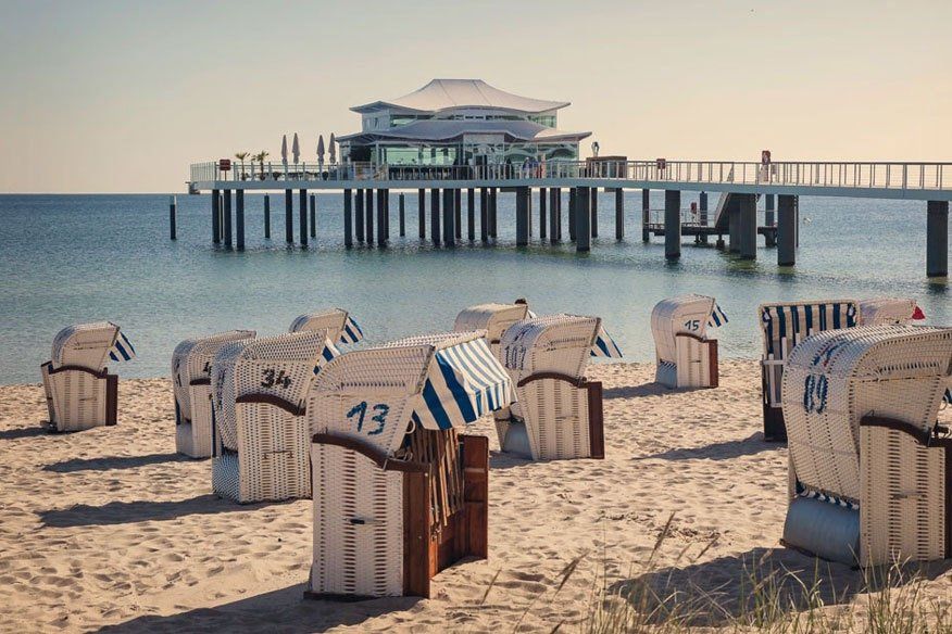 Eine Reihe von Strandstühlen an einem Strand mit einem Pier im Hintergrund.