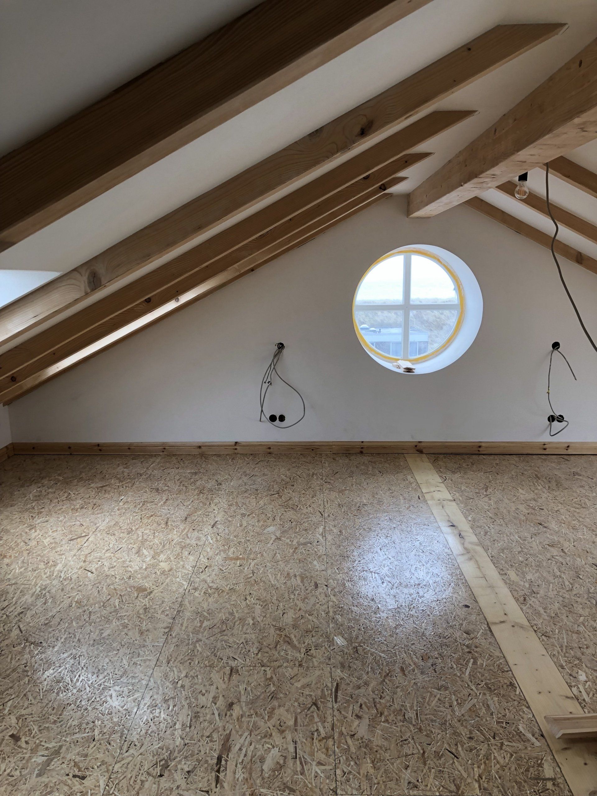 Ein leerer Dachboden mit einem runden Fenster und Holzbalken