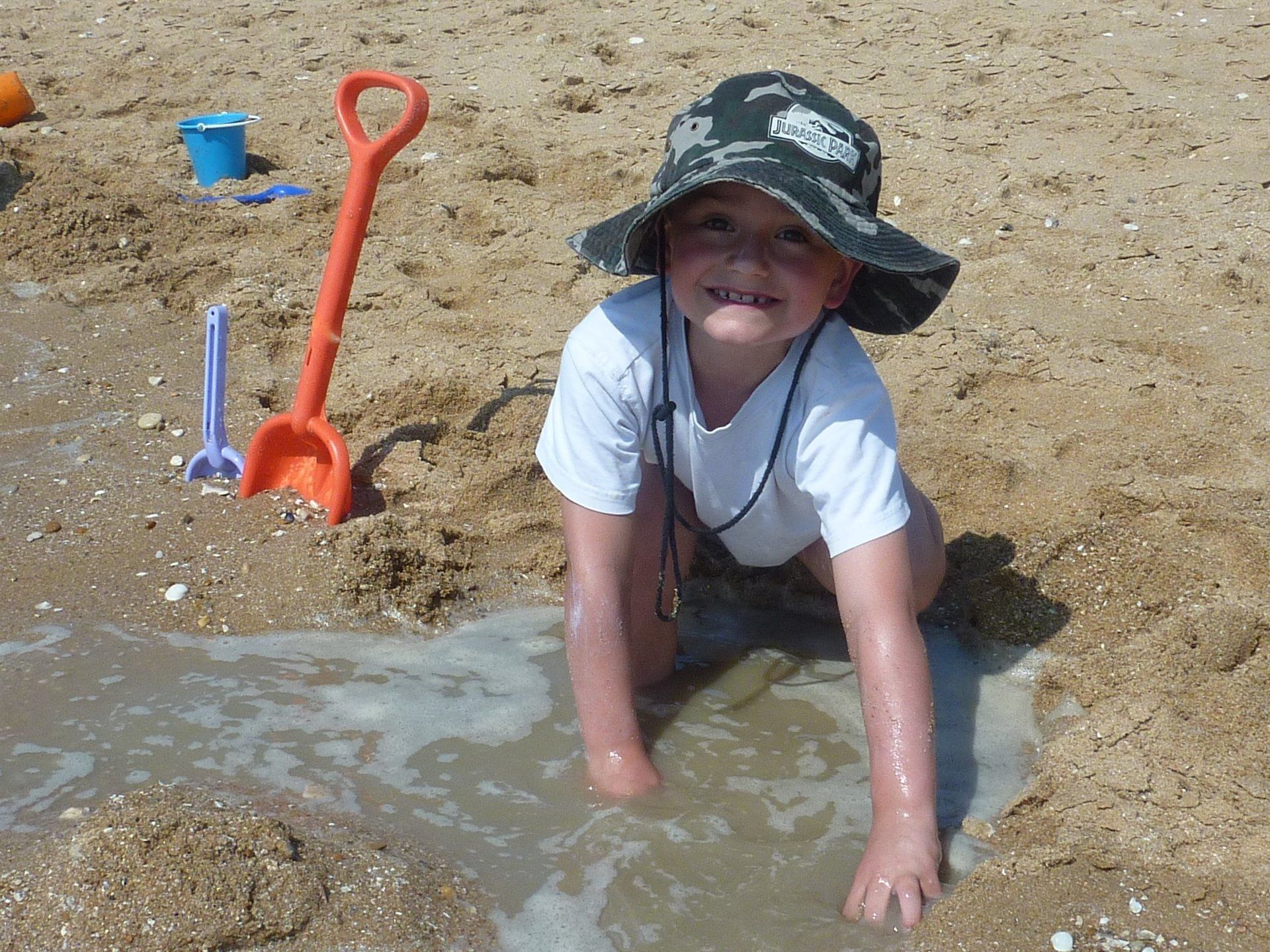 a boy digging a hole in the sand at the beach with seawater pouring in
