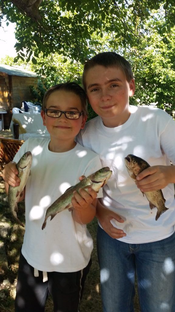 two boys wearing white t-shirts holding three trout they have caught