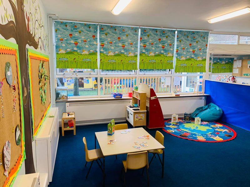 A brightly coloured nursery with a blue carpet and patterned blinds, with toys and children's furniture