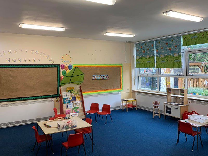 Room in a nursery with a blue carpet and red plastic chairs around small tables