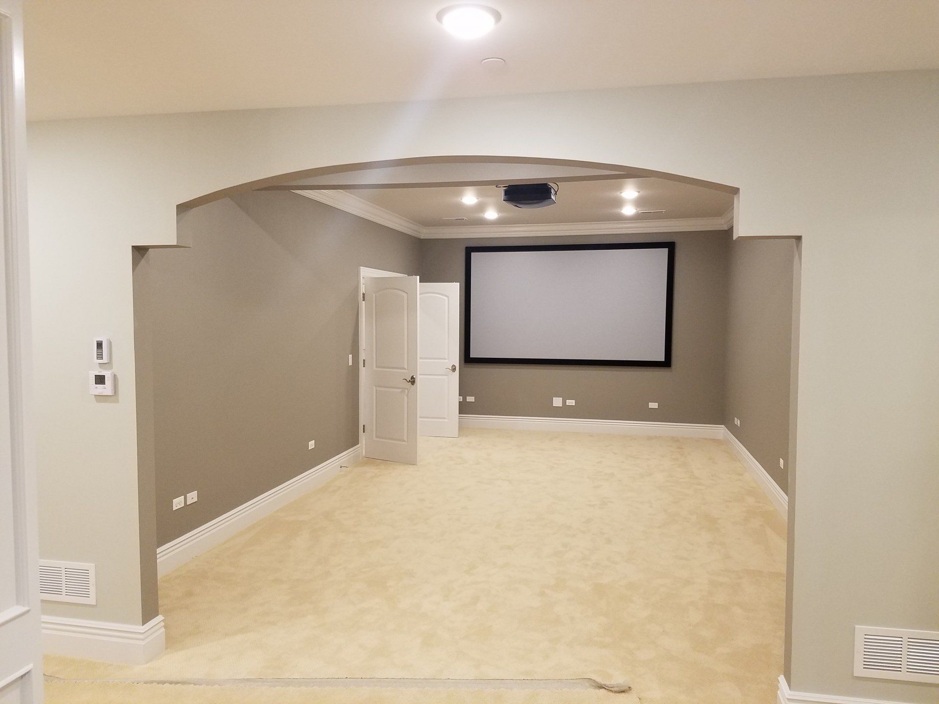 Movie theater room with white screen, projector, tan carpet, and gray walls.