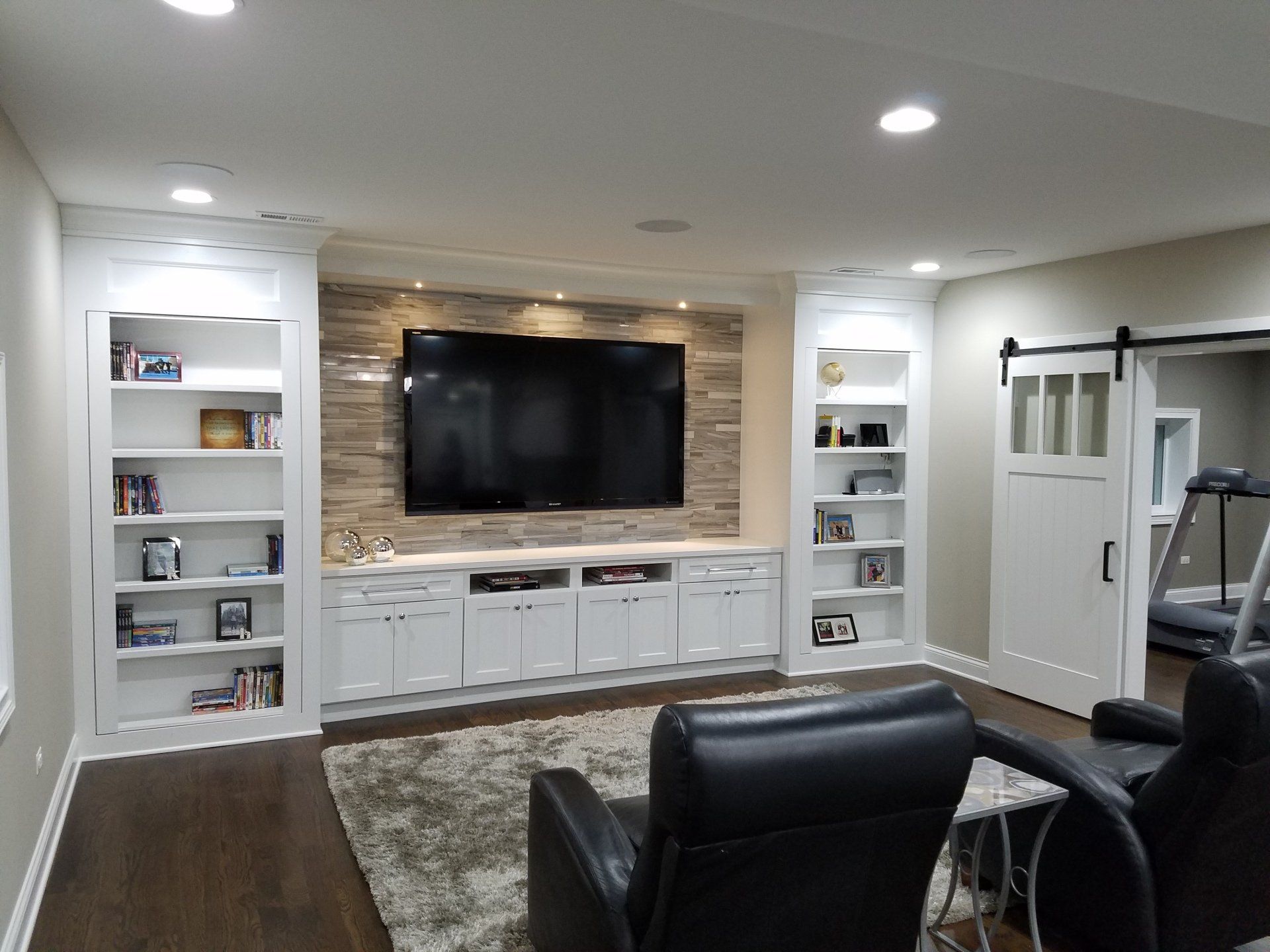 A finished basement entertainment center with a TV, built-in cabinets, and a sliding barn door.