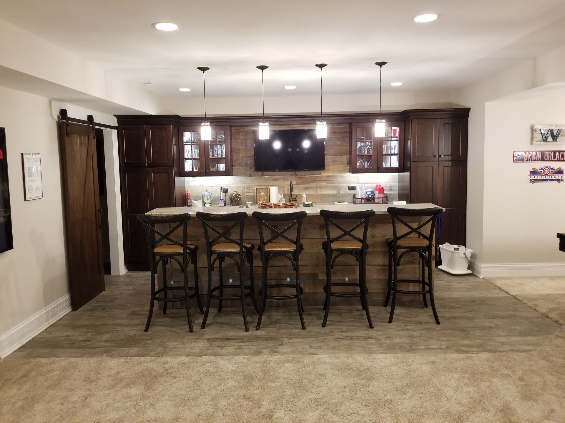 Basement bar with dark wood cabinets, stone backsplash, and six bar stools.