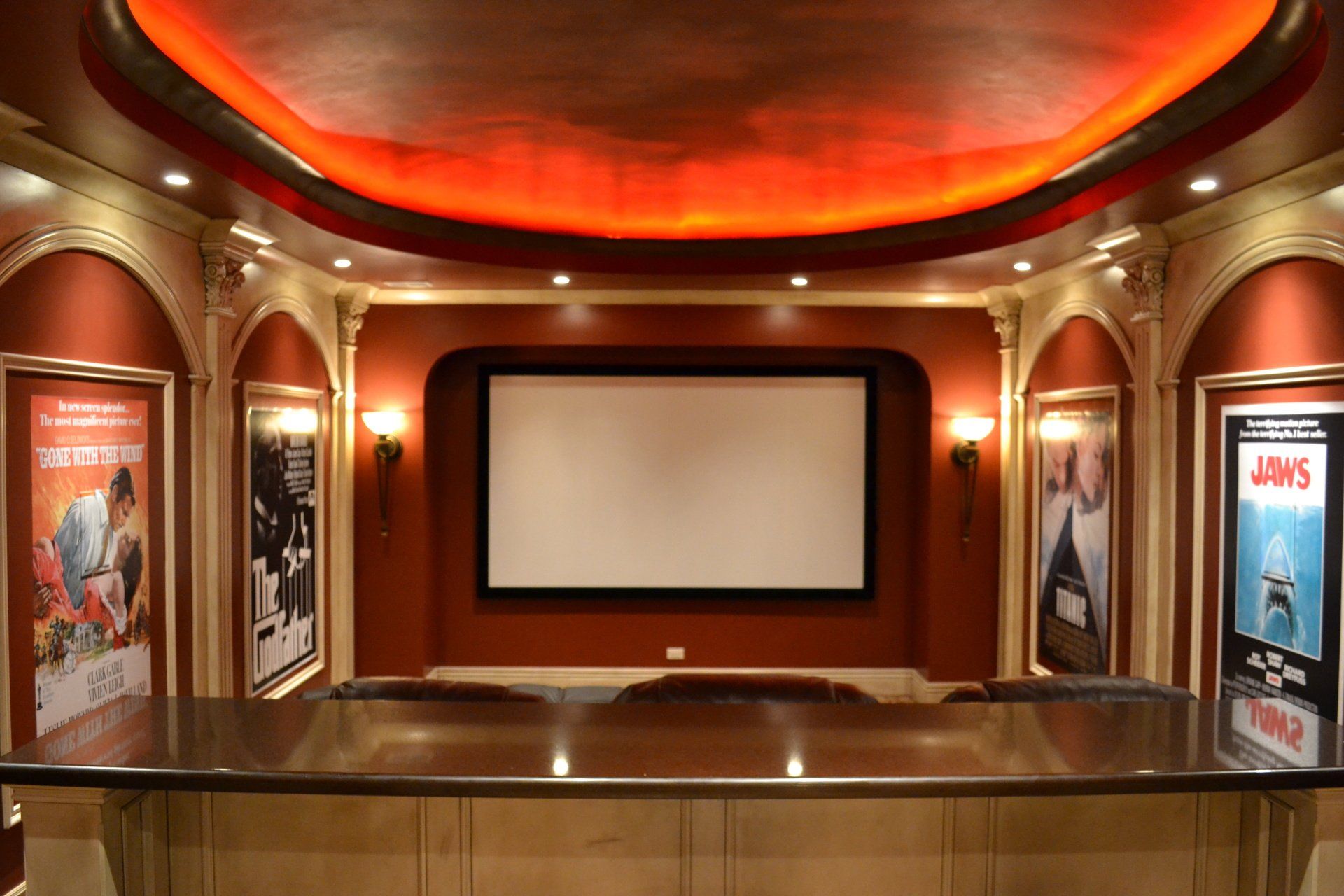 Home theater with screen, movie posters, red walls, and bar seating.