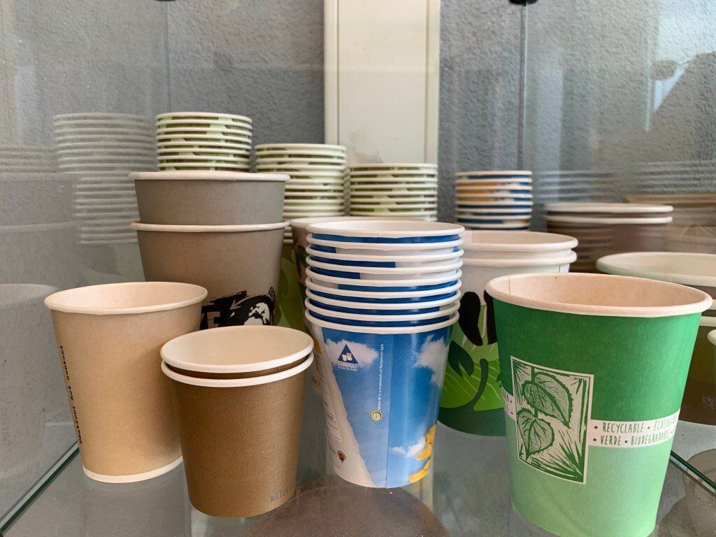 A variety of bioplastic paper cups are stacked on top of each other on a glass table.