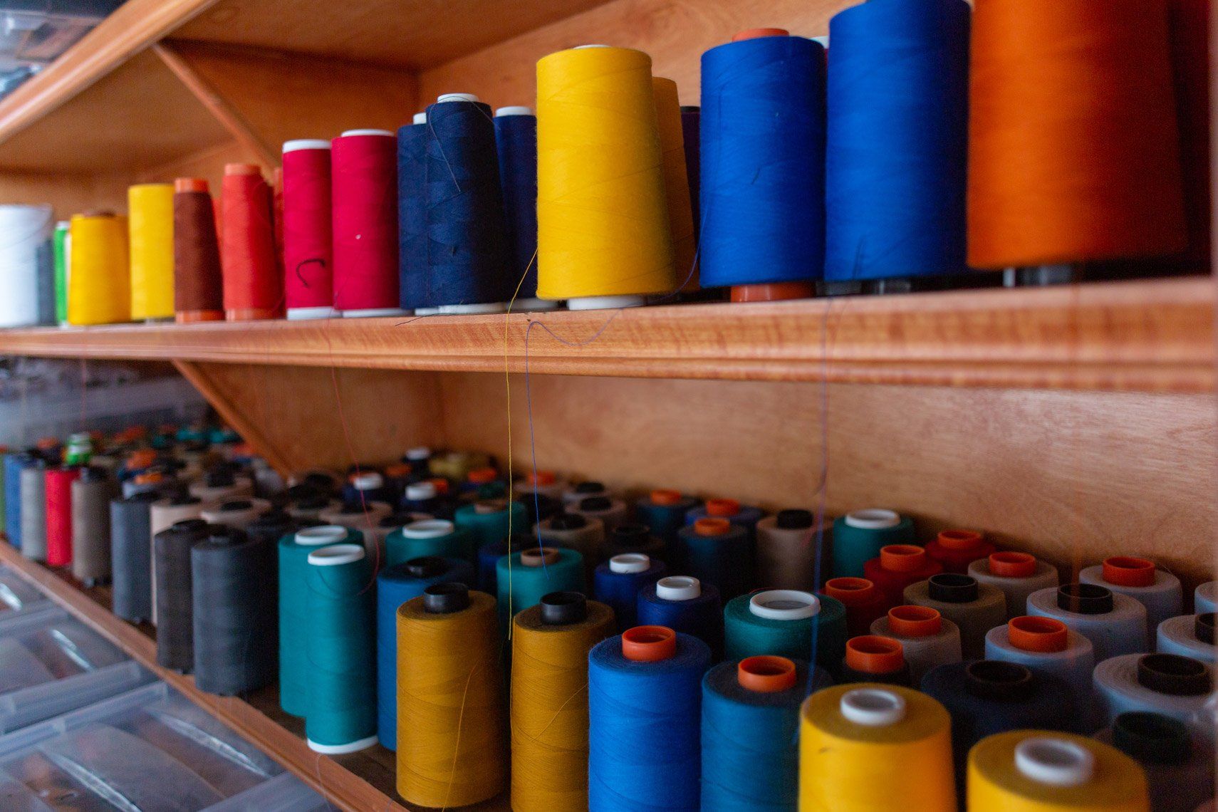 There are many different colored spools of thread on the shelves.