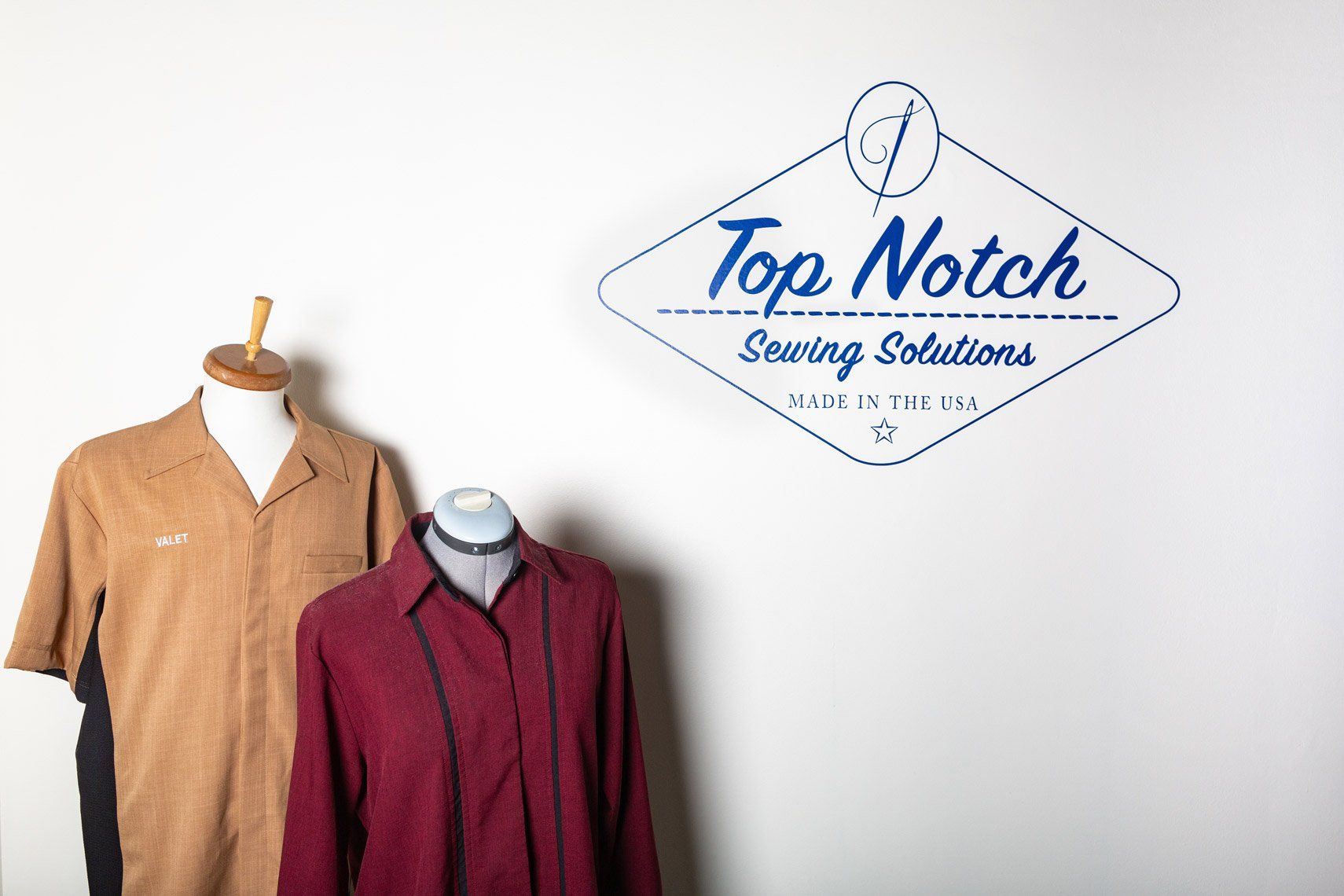 Two shirts on a mannequin in front of a sign that says top notch sewing solutions