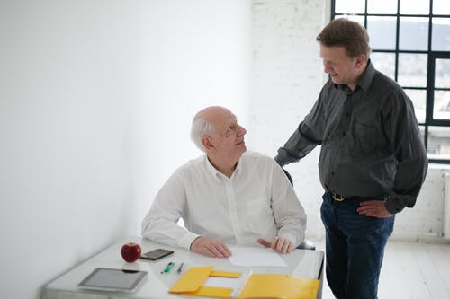 older man sitting younger man touching his back talking