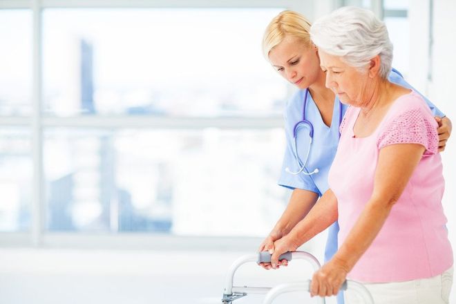 Young female nurse helping senior woman with walker in nursing home. Horizontal shot.