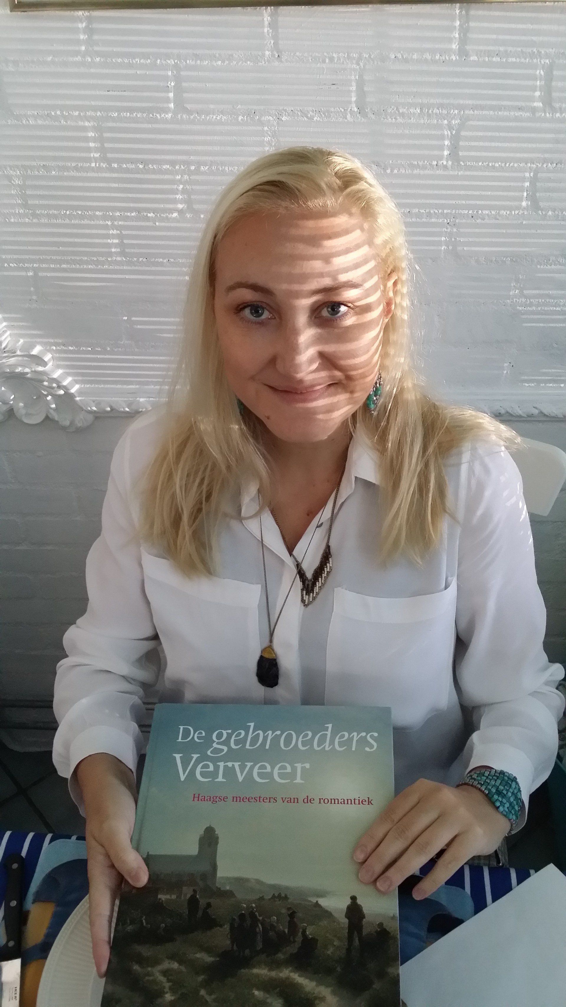 Een persoon in een witte blouse houdt een boek vast met de titel 