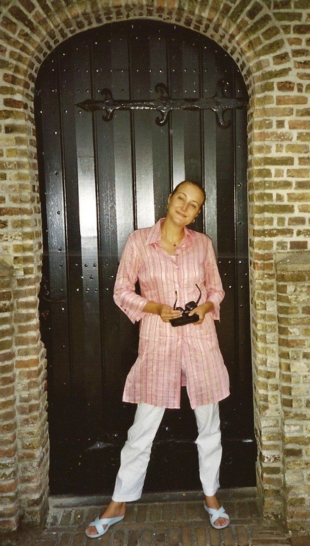 Een persoon in een roze shirt en witte broek staat 's nachts in een bakstenen doorgang en houdt een camera vast.
