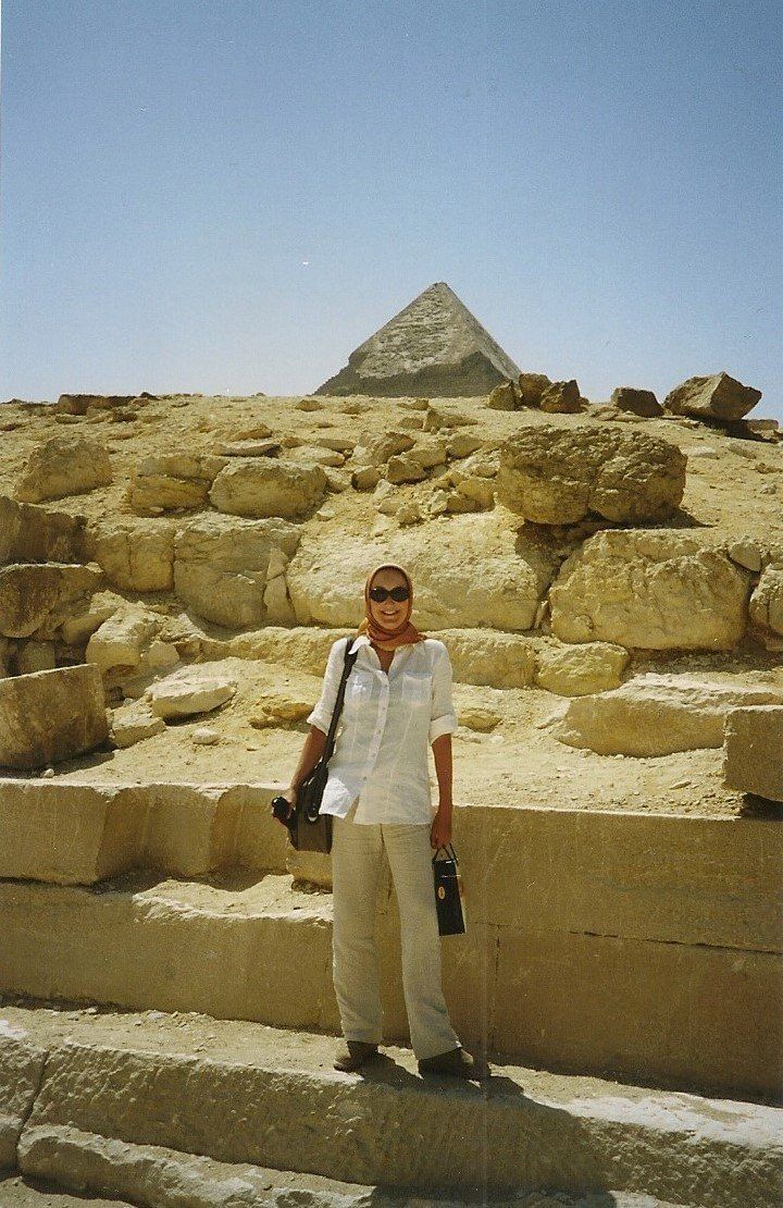 Persoon staand voor de Grote Piramide van Gizeh, met stenen blokken op de voorgrond.