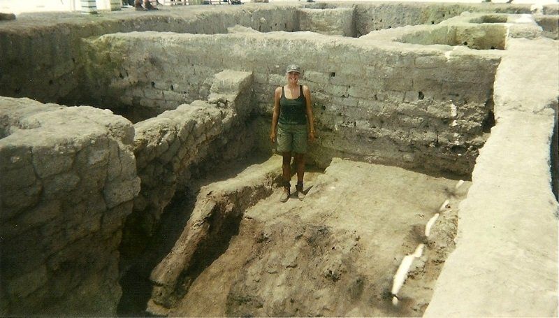 Persoon staand op een archeologische opgraving met stenen muren en greppels.