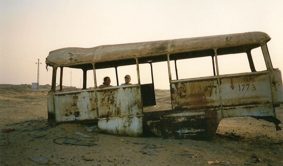 Een verroeste, verlaten bus in een stoffig veld bij zonsondergang.