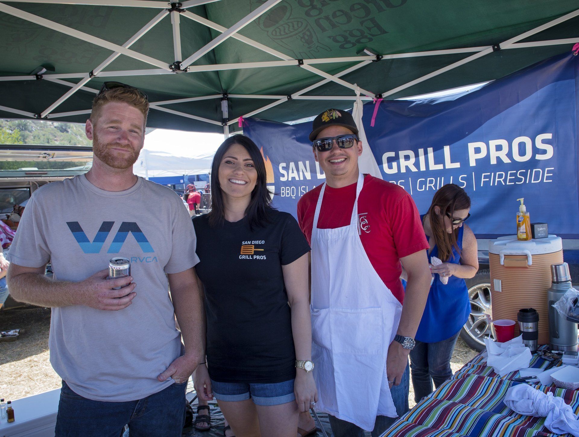 Three people are posing for a picture in front of a grill pros tent.