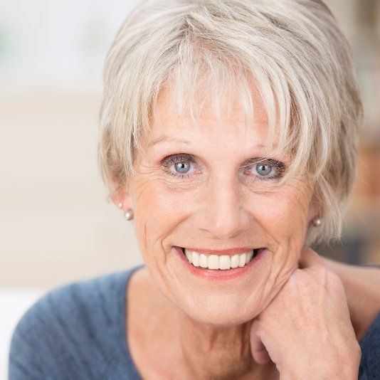 A close up of a woman 's face smiling with her hand on her chin.