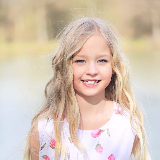A little girl with long blonde hair is smiling for the camera.