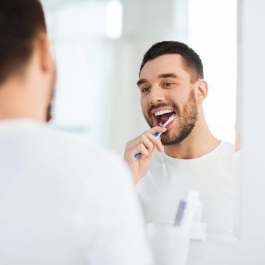 A man is brushing his teeth in front of a mirror.