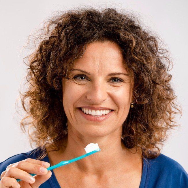 A woman with curly hair is brushing her teeth with a blue toothbrush