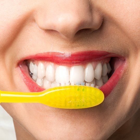 A woman is brushing her teeth with a yellow toothbrush.