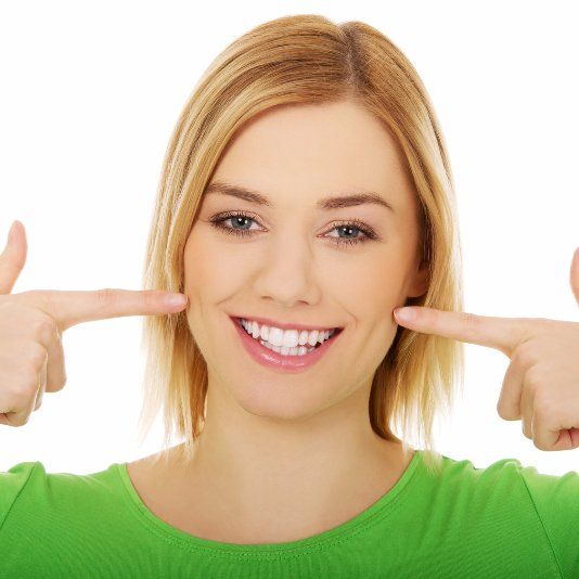 A woman in a green shirt is smiling and pointing at her teeth