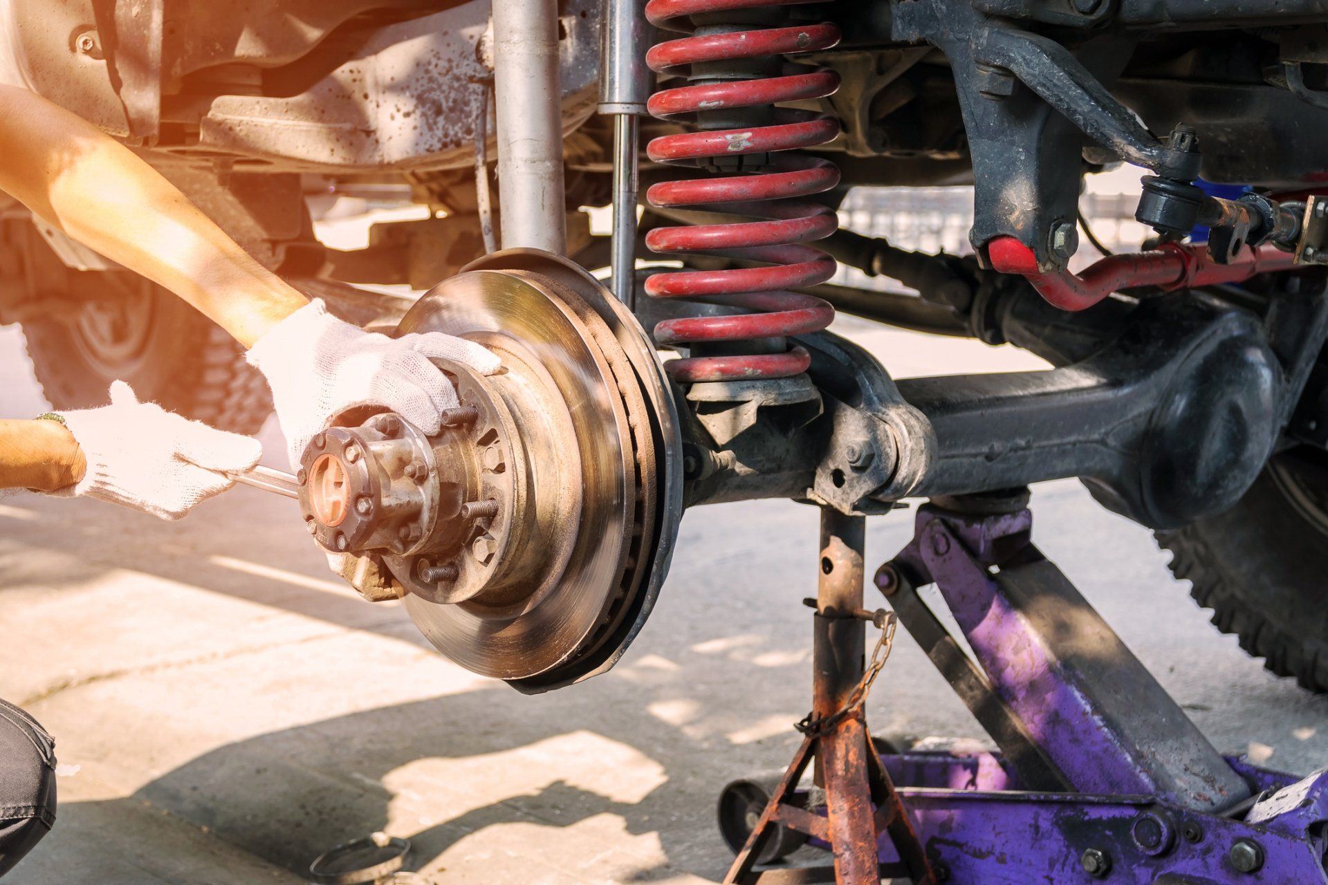 Mechanic working on a car's brake system, using a jack for support.