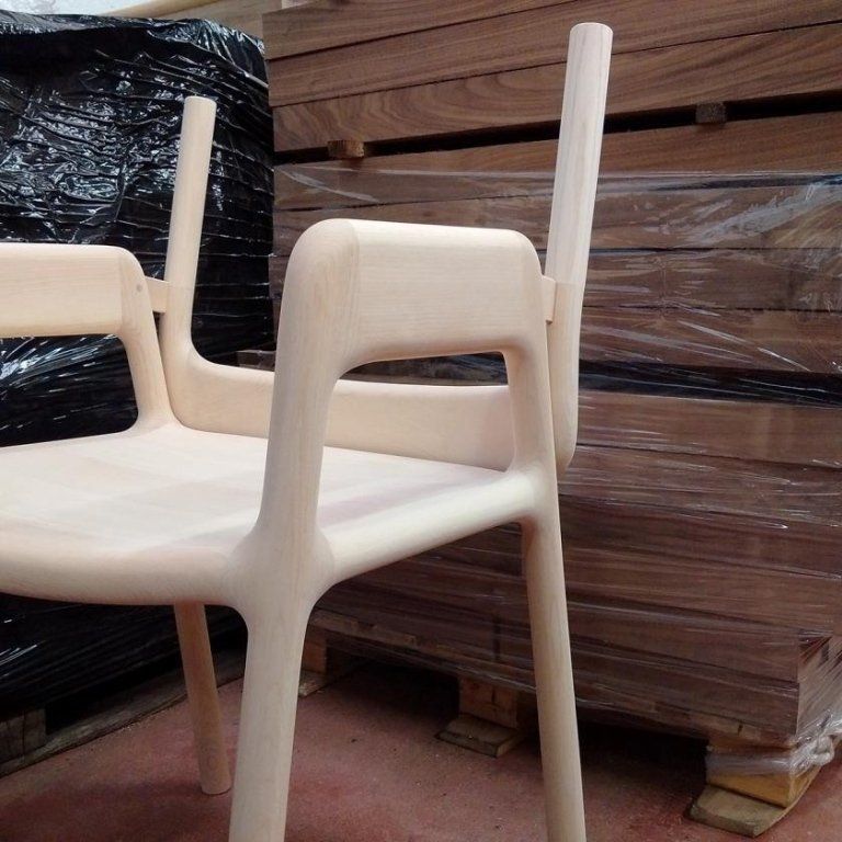 Sedie di plastica bianca impilate e avvolte nella plastica, vicino a pallet di legno in un magazzino.