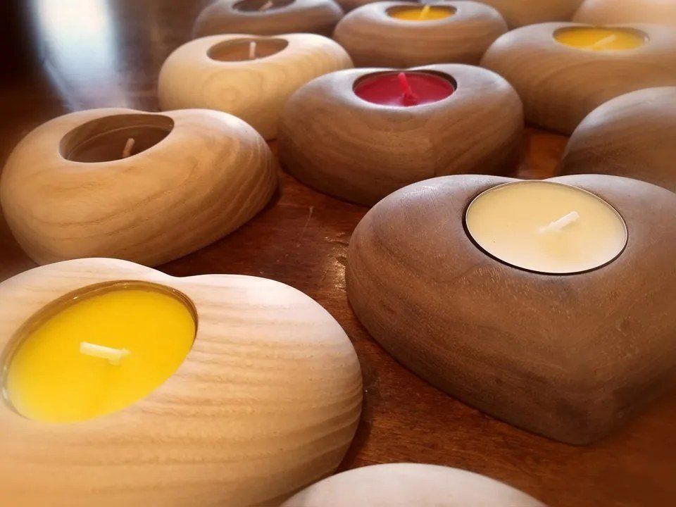 Su un tavolo, assortiti portacandele in legno con lumini accesi di colore giallo, bianco e rosso.