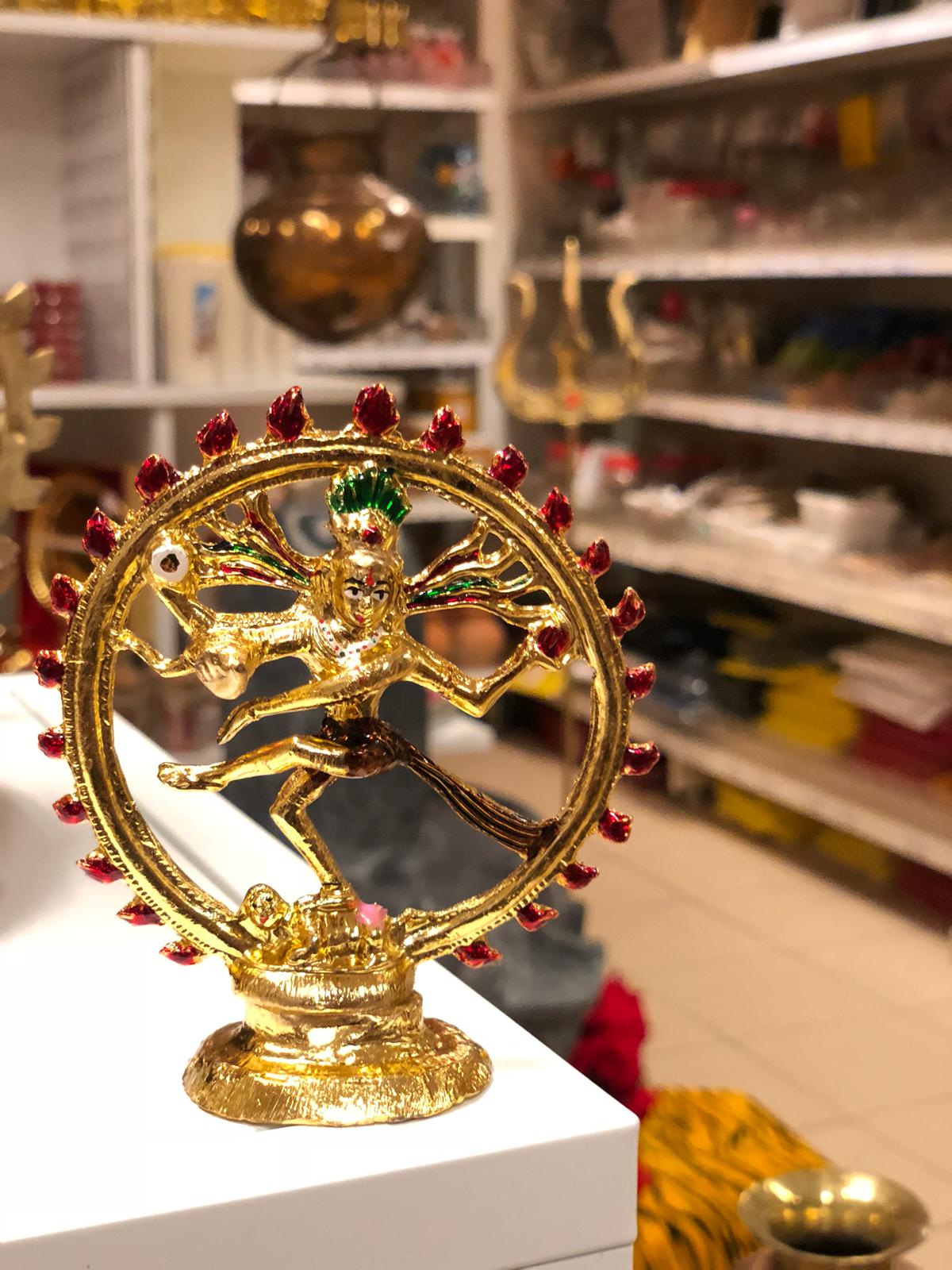 Op een tafel in een winkel staat een gouden beeld van een dansende godheid.