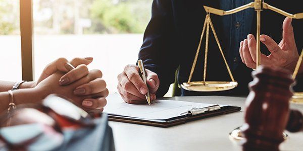 A lawyer is sitting at a table with a clipboard and a scale of justice.