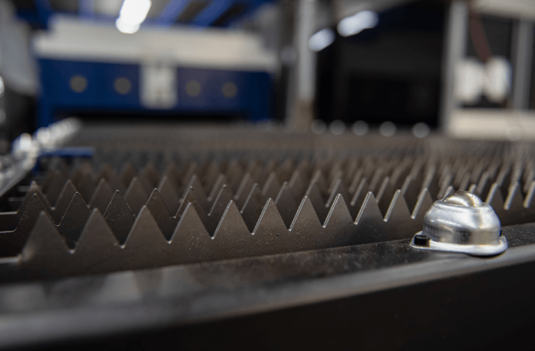 Close-up of a metal industrial cutting surface with sharp triangular teeth and a silver bolt