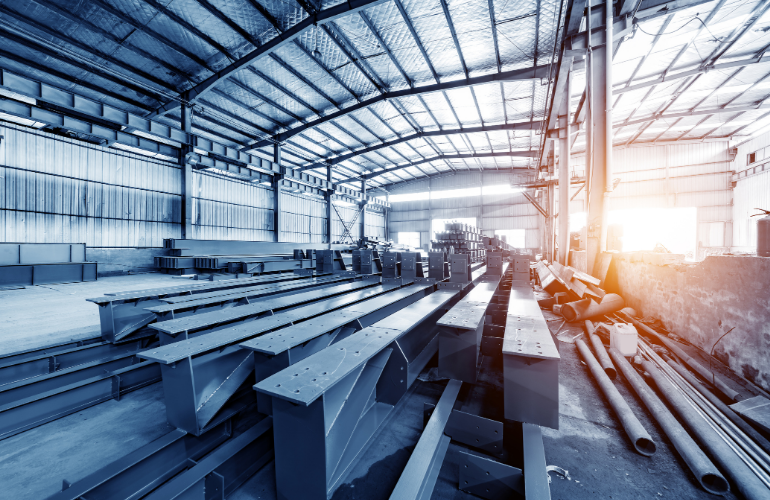 Steel beams stacked inside a sunlit industrial warehouse